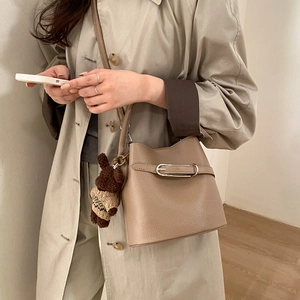 Sac seau beige chic avec texture litchi et un charm d'ours brun sur un manteau beige