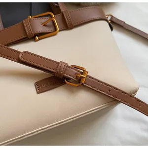 Dettaglio di tracolle regolabili in pelle marrone con fibbie dorate su borsa beige