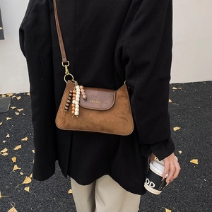 Détail d'un sac sous les aisselles en daim marron avec rabat en cuir et gland perlé
