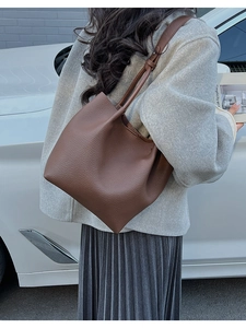 Detail of a brown lychee pattern leather tote bag carried over the shoulder by a model