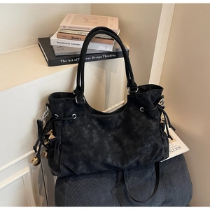 Detail of vintage matte black tote bag with drawstring and metal ball charms on a soft stool