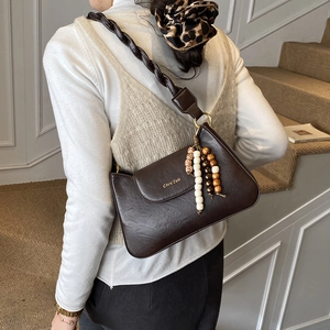 Détail d'un sac porté épaule marron foncé avec bandoulière tressée et perles en bois