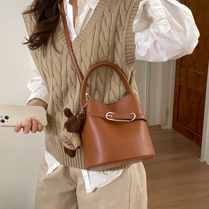 Détail d'un sac seau marron avec motif litchi et un petit porte-clés ours en peluche à carreaux
