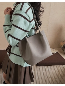 Close-up of textured grey leather bucket bag on a wooden bench with natural light