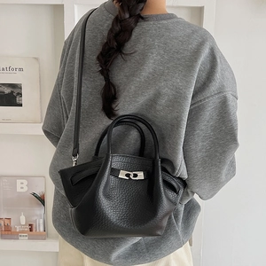 Détail du sac seau en cuir noir avec fermoir argenté porté par un mannequin en salle