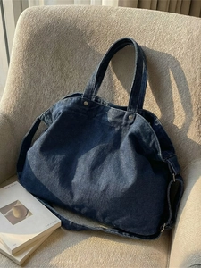 Large dark blue washed denim tote bag with adjustable strap on a cozy beige sofa