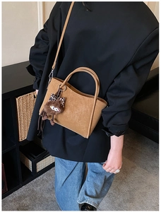 Close-up of brown suede bucket bag featuring round handle and plush monster charm