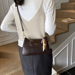 Détail du sac à bandoulière marron mat vintage avec logo et pendentif perlé élégant