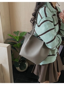 Detailed view of grey pebble leather bucket bag carried by model in home setting