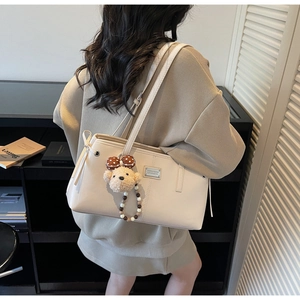 Detail of cream PU tote bag featuring a silver logo plate and cute plush bear charm