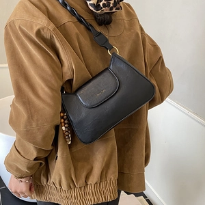 Détail d'un sac bandoulière noir avec bandoulière tressée et pampille à perles