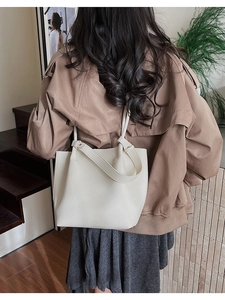 Close-up of minimalist cream bucket bag in lychee pattern leather worn by model