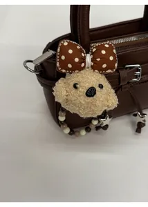 Detail of cute beige plush dog charm with polka dot bow on dark brown leather handbag