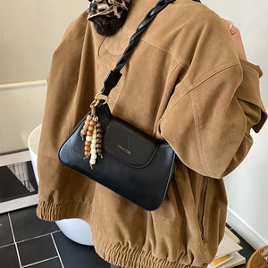 Détail du sac bandoulière en cuir noir avec breloque perlée et bandoulière tressée