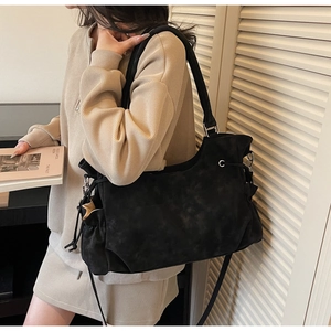 Detail view of black suede tote bag featuring adjustable side drawstring and strap