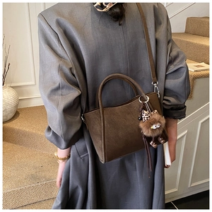 Detail of dark brown suede bucket bag with plush charm on a grey wool coat outfit