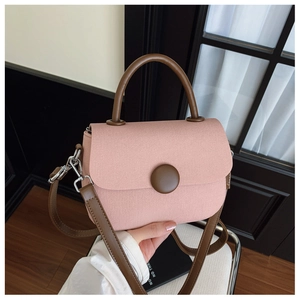 Detalle del bolso bandolera en contraste rosa y marrón con botón redondo y herrajes plateados