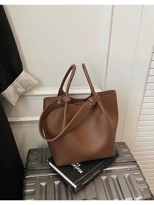 Detail of brown litchi pattern leather bucket bag placed on luggage for travel context