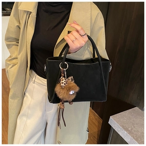 Detail of black matte bucket bag with cute plush charm held by model in trench coat