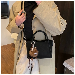Detail of matte black bucket bag with leopard bow charm on a beige trench coat