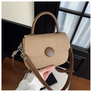 Detalle de bolso tipo silla en lona caqui con correa de cuero marrón y hebilla circular