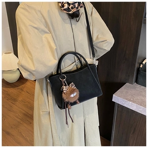 Detail of matte black bucket bag with plush monster charm on model wearing beige coat
