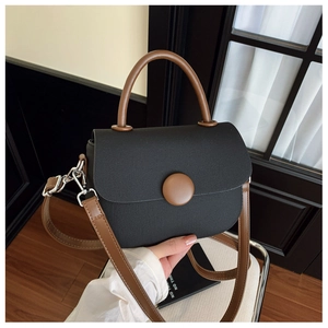Detalle de bolso bandolera negro con asa marrón y hebilla de metal plateado