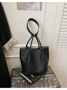 Close-up of black pebble leather bucket tote bag texture and long handles on a luggage prop