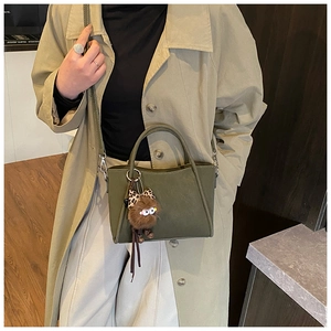 Olive green bucket bag with plush monster charm paired with a beige trench coat