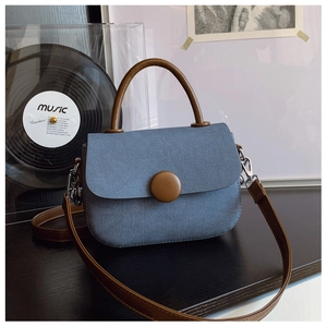 Detalle de bolso azul texturizado con asa redonda marrón y correa de cuero ajustable