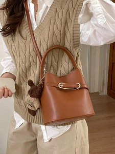 Sac seau en cuir litchi marron avec pendentif ours porté par un mannequin en intérieur