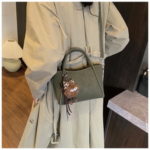 Olive green bucket bag with a cute plush monster pendant shown on a model's shoulder