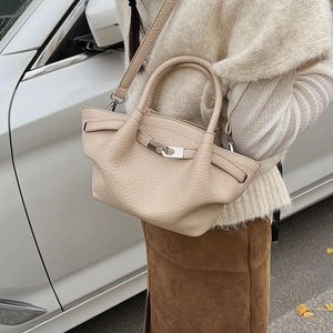 Détail du sac seau en cuir beige avec fermoir rotatif argenté et doubles poignées de main