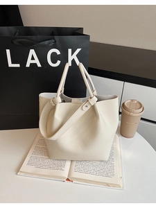 Chic beige lychee leather bucket bag displayed on an open book with coffee cup