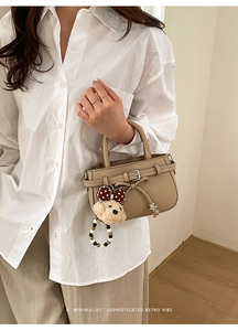 Detail der khakifarbenen Ledertasche mit Schleifenschnalle und Plüschbär-Anhänger-Dekor