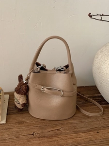 Sac seau chic en cuir litchi marron clair avec breloque ours sur une table en bois