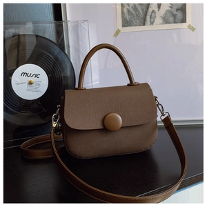 Detalle de bolso vintage de tela marrón con asa de cuero y botón redondo decorativo