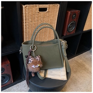 Detailed view of dark green bucket bag with textured leather and plush monster charm