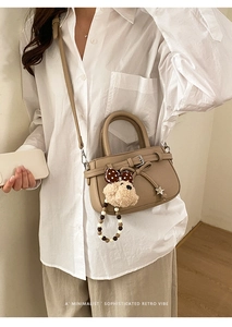 Detail of retro khaki crossbody bag with decorative bow and plush pendant on white shirt