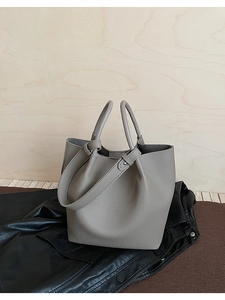 Detail of grey bucket bag with lychee texture on leather jacket and wooden wall