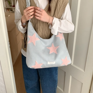 Detail of light blue suede shoulder bag featuring pink plush stars and a white brand label