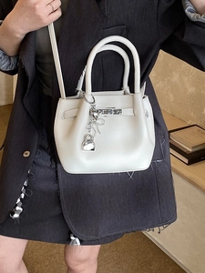 Sac seau en cuir blanc avec finitions argentées et breloque cœur porté par mannequin