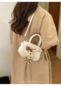 Schicke cremefarbene Ledertasche mit Schleifenanhänger und Bärenanhänger am Trenchcoat