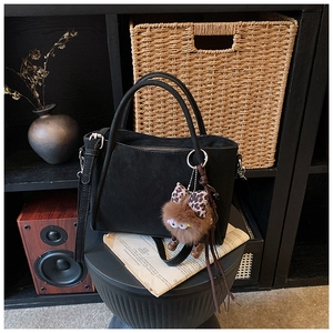 Detail of black frosted bucket bag with a plush charm on a minimalist shelf