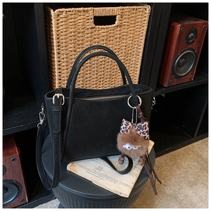 Detail of black matte bucket bag with double handles and a cute leopard bow charm