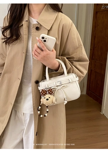 Detailed shot of a white lychee leather mini handbag with a cute plush puppy pendant