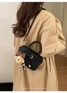 Detail of black litchi grain leather handbag with a plush bear charm and crossbody strap