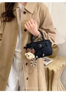 Detail of black lychee grain handbag featuring silver buckle and bow knot with plush charm