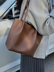 Minimalist dark brown lychee leather bucket tote bag worn by a model in outdoor setting