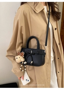 Detail der schwarzen Lederhandtasche mit Schleife und Bär-Anhänger am Trenchcoat
